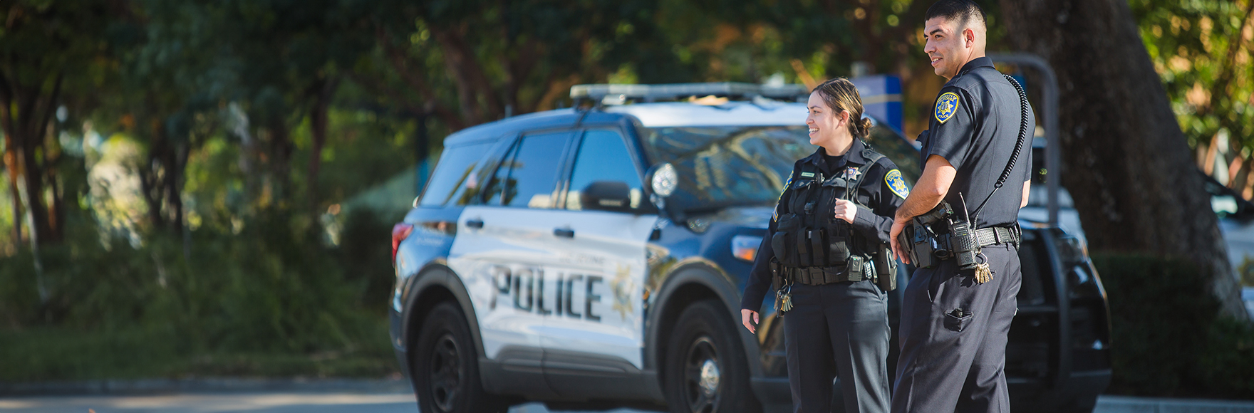 Officers smiling off-camera in front of a police car on UCI Ring Road